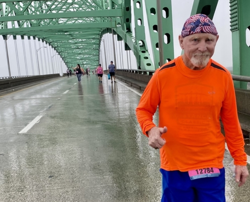 An elderly man in an orange shirt runs across a bridge on a rainy day.