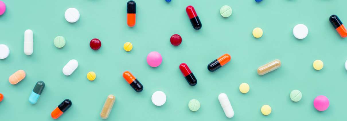 A colorful display of generic pills are scattered about on a mint green background.