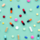 A colorful display of generic pills are scattered about on a mint green background.