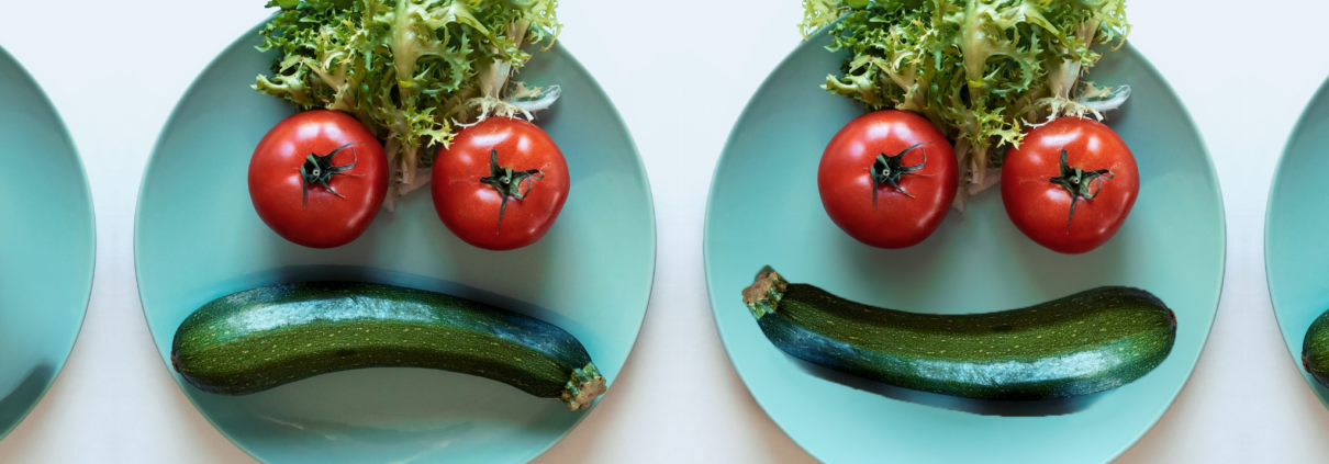 Two turquoise dinner plates sit side by side on a plain background. A cucumber, two tomatoes and lettuce on each plate are arranged to make a face. One face is smiling; the other is frowning.