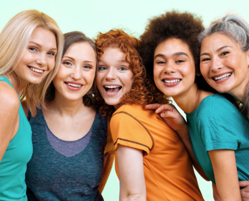 5 ethinically diverse women in their 40s and 50s lean toward each other and pose, smiling, for the camera.