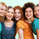 5 ethinically diverse women in their 40s and 50s lean toward each other and pose, smiling, for the camera.