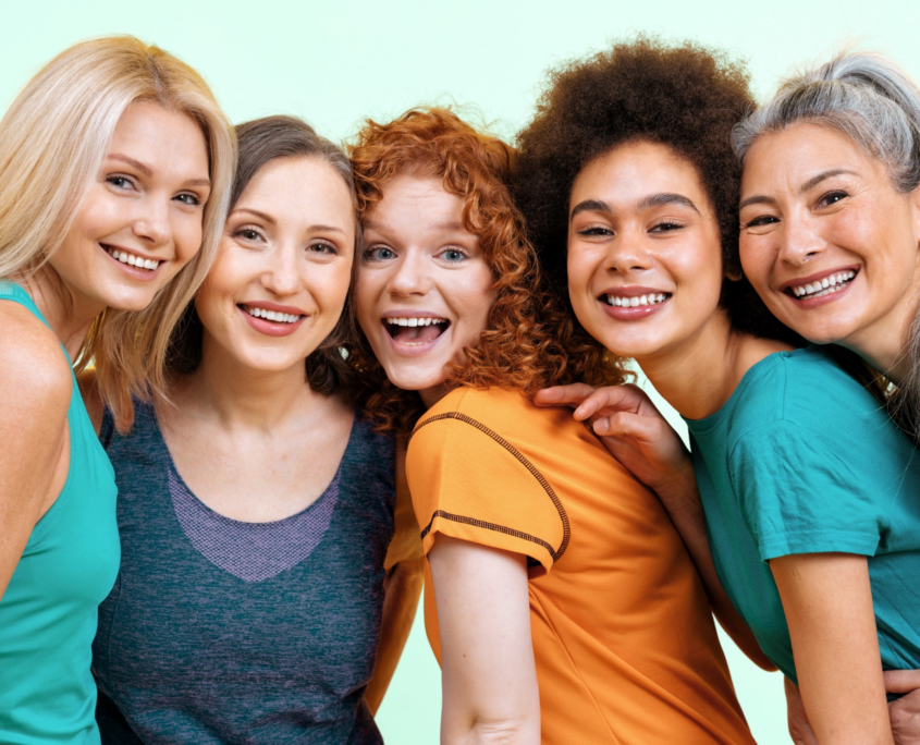 5 ethinically diverse women in their 40s and 50s lean toward each other and pose, smiling, for the camera.