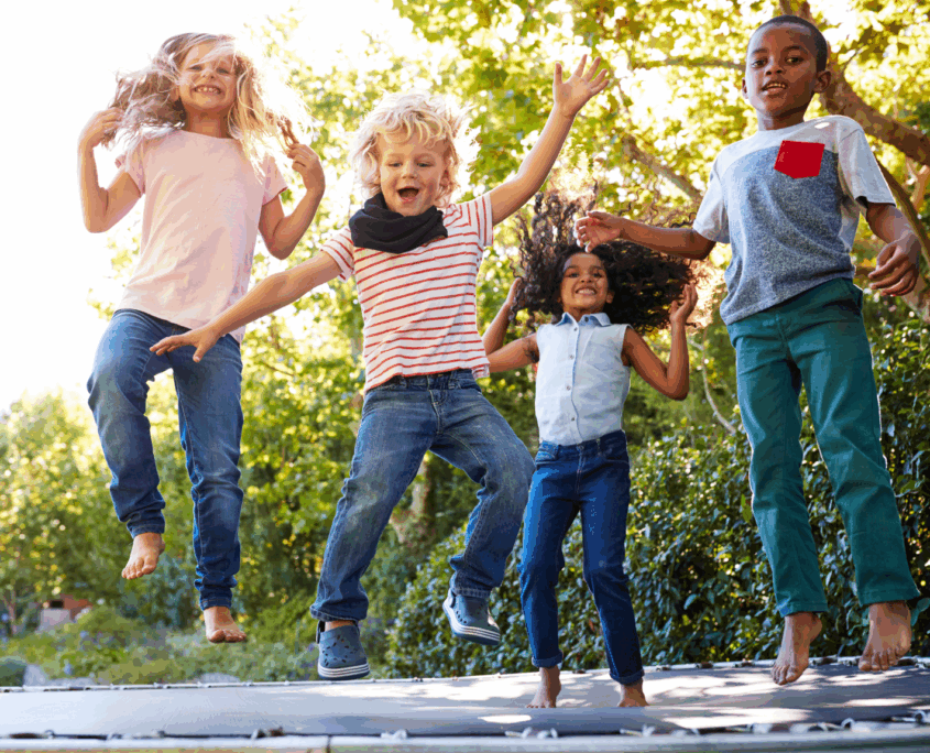 Four elementary-age kids jump up and down on a trampoline and laugh and smile at the camera.