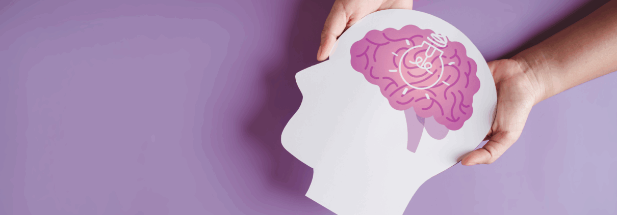 The image is mostly a lilac-covered background with two white hands holding a one-dimensional cutout of a head with a brain showing in pink colors.