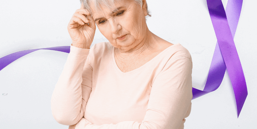An elderly white woman with short gray hour and wearing a light-colored peach top with long sleeves is looking down and holding her right hand to her head, as if in thought. A purple ribbon design is part of the background image.