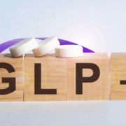 BW_food_GLP1 New Four small brown blocks, similar to Scrabble tiles sit next to each other and spell out GLP-1. Three small white pills sit on top of the blocks and an image of a purple ribbons winds its way around the blocks.