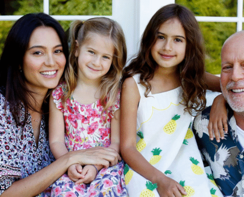 Actor Bruce Willis faces the camera on the right next to his two daughters and his wife, Emma, on the far left. All are smiling and wearing tropical shirts.