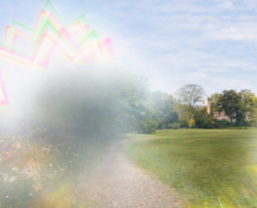 A distorted image shows how a person might see a migraine aura. A scene of a green field with green trees in the distance is disturbed by a fuzzy dark shape on the left surrounded by colorful zigzags.