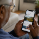 We see the blurry side of an older man from behind him as he looks down at a Facebook page on his smartphone he is holding in both hands.
